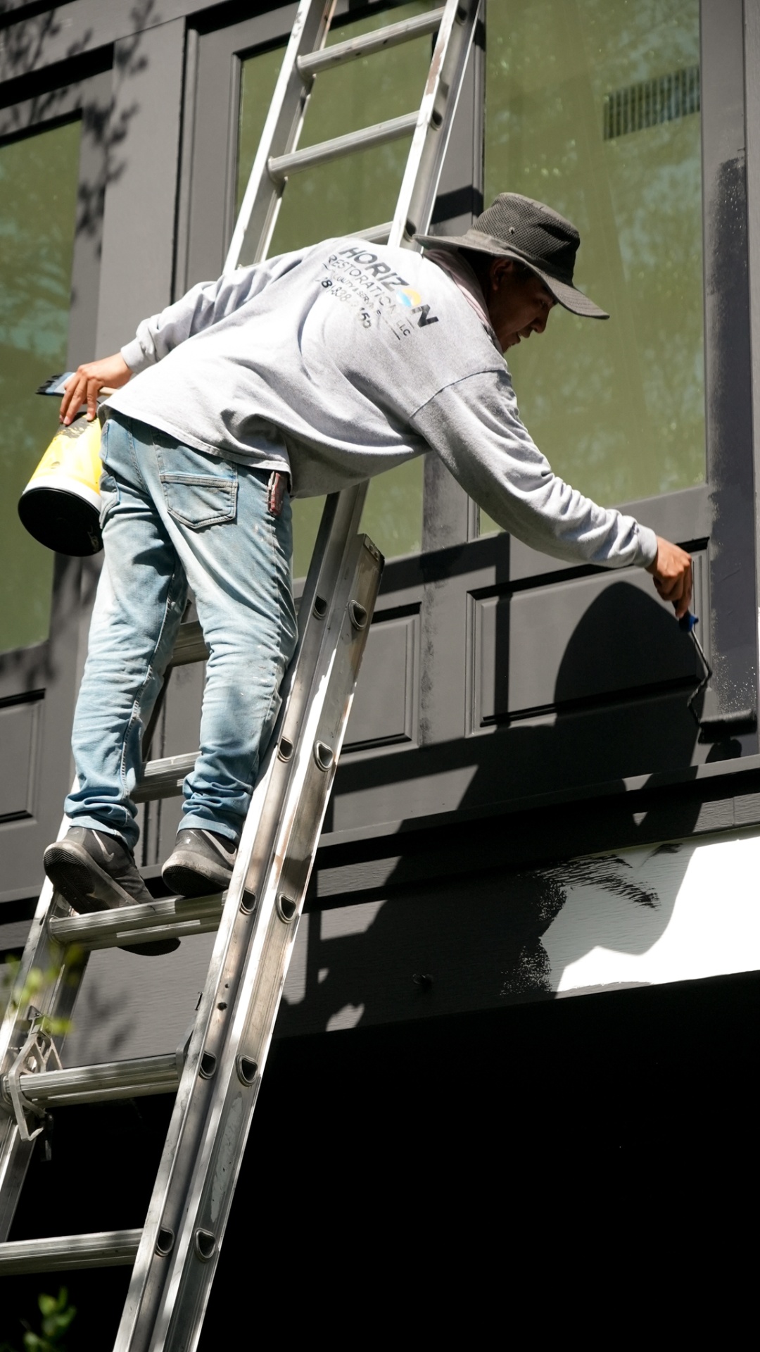 Painter on a ladder rolling exterior trim by hand
