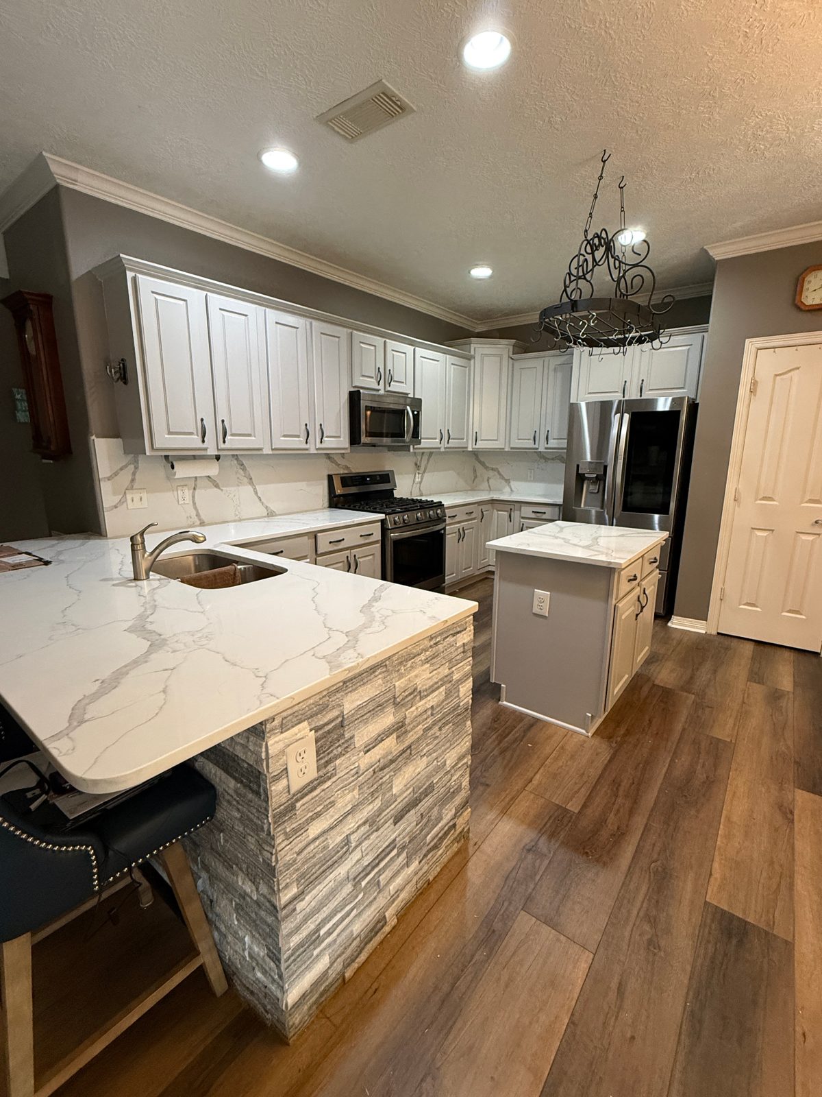 Freshly refinished white kitchen cabinets with marble countertops and a stone island